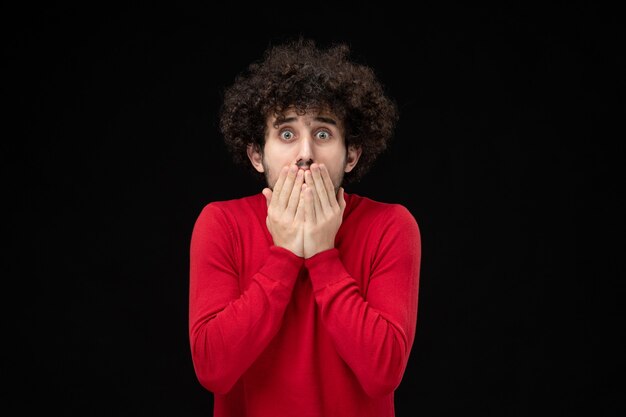 Vue de face du jeune homme en chemise rouge sur mur noir