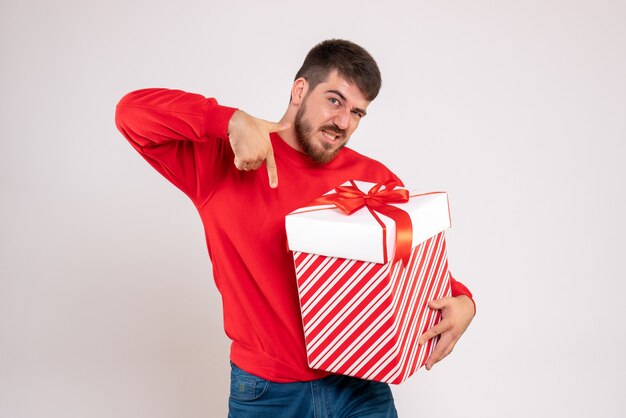 Vue de face du jeune homme en chemise rouge tenant le cadeau de Noël dans la boîte sur le mur blanc