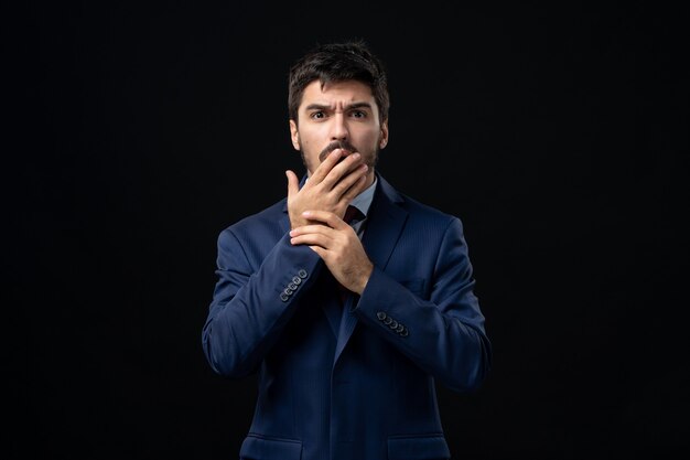 Vue de face du jeune homme choqué en costume sur un mur sombre isolé