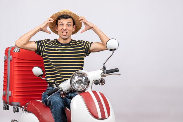 Vue de face du jeune homme en colère avec un chapeau de paille sur un cyclomoteur