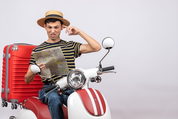 Vue de face du jeune homme confus avec chapeau de paille sur l'emplacement de recherche de cyclomoteur sur la carte