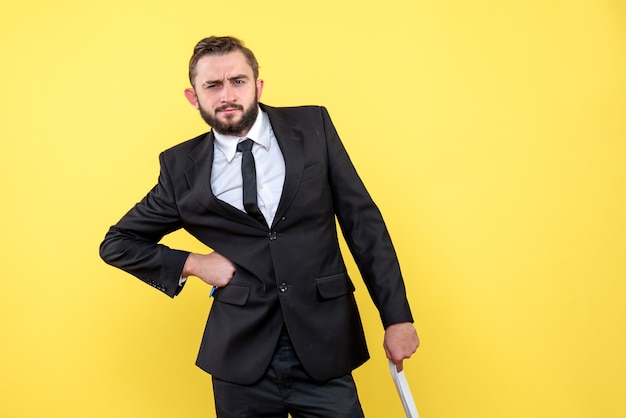 Vue de face du jeune homme en costume noir sérieusement à la recherche d'une main sur le côté et autre tenant des feuilles de papier vierges sur jaune