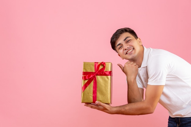 Vue de face du jeune homme donnant un cadeau de Noël à quelqu'un sur le mur rose