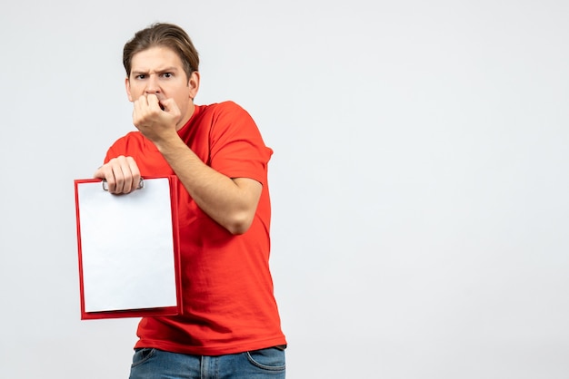 Vue de face du jeune homme effrayé en chemisier rouge tenant un document sur fond blanc