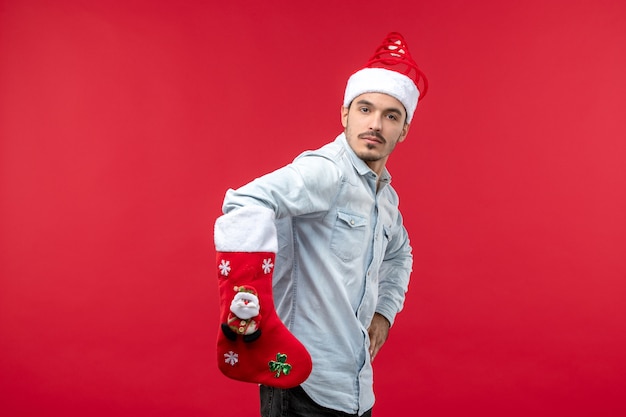 Vue de face du jeune homme avec grosse chaussette de Noël sur mur rouge