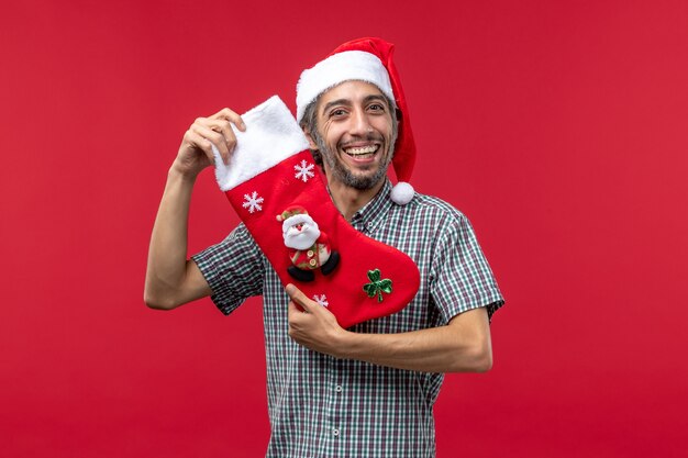 Vue de face du jeune homme avec une grosse chaussette de Noël sur le mur rouge