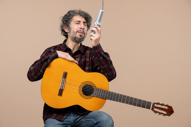 Vue de face du jeune homme avec guitare chantant au micro sur le mur rose