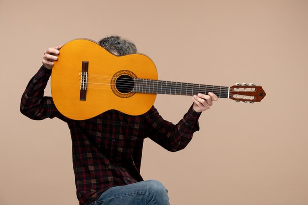 Vue de face du jeune homme avec guitare sur le mur rose