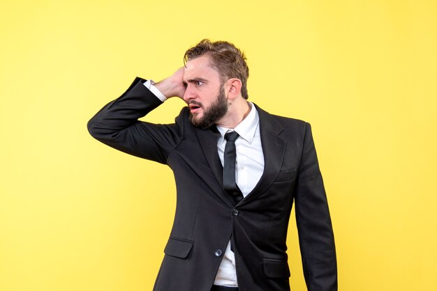 Vue de face du jeune homme homme d'affaires décomposé et touche la tête avec la main sur jaune