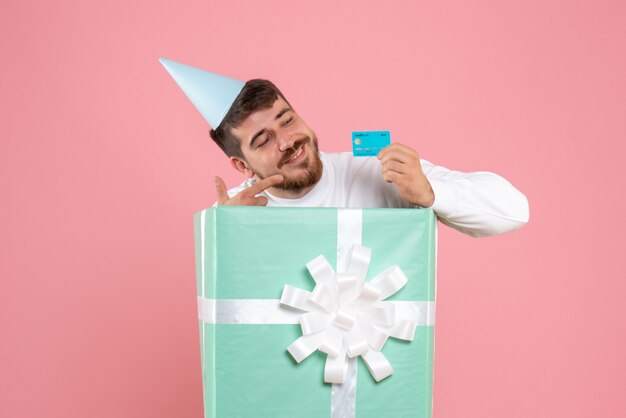 Vue de face du jeune homme à l'intérieur de la boîte actuelle tenant une carte bancaire sur le mur rose