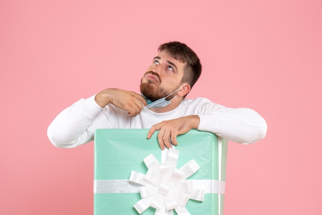 Vue de face du jeune homme à l'intérieur de la boîte présente décoller son masque sur mur rose