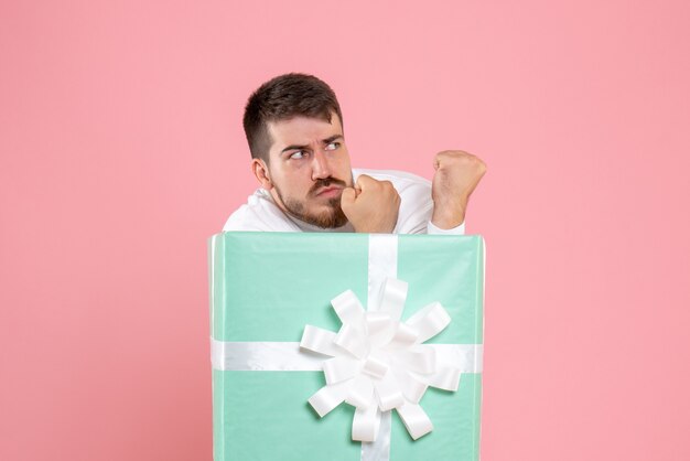 Vue de face du jeune homme à l'intérieur de la boîte présente sur le mur rose