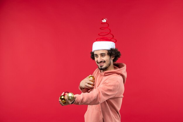 Vue de face du jeune homme avec des jouets d'arbre de Noël sur mur rouge