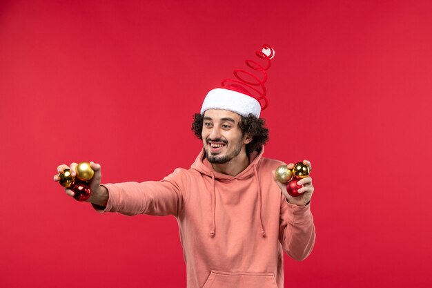 Vue de face du jeune homme avec des jouets d'arbre de Noël sur mur rouge