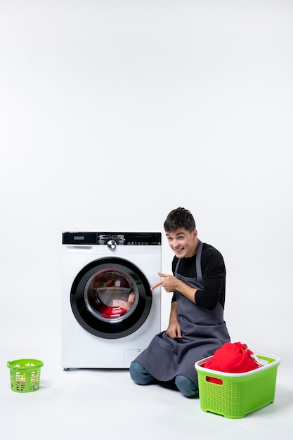 Photo gratuite vue de face du jeune homme lavant les vêtements à l'aide d'une machine à laver sur un mur blanc