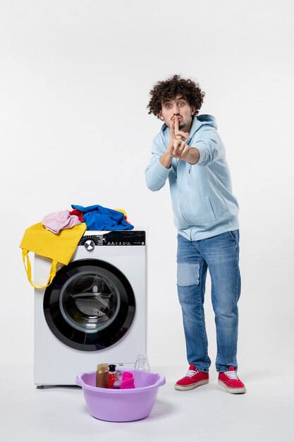 Vue de face du jeune homme avec lave-linge et vêtements sales sur mur blanc