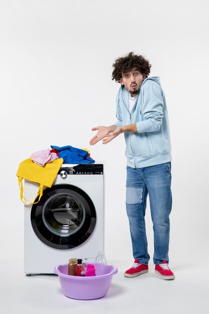 Vue de face du jeune homme avec lave-linge et vêtements sales sur mur blanc