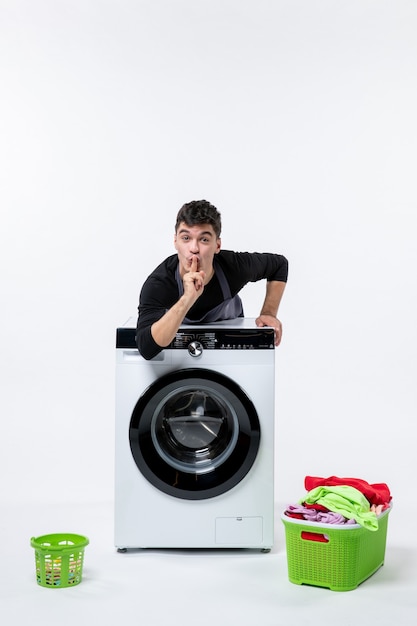 Vue de face du jeune homme avec lave-linge et vêtements sales sur mur blanc