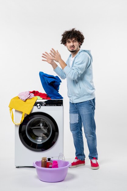 Vue de face du jeune homme avec lave-linge et vêtements sales sur mur blanc