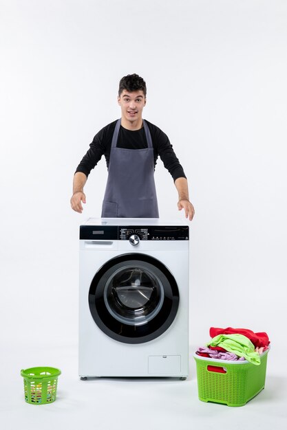 Vue de face du jeune homme avec lave-linge et vêtements sales sur mur blanc