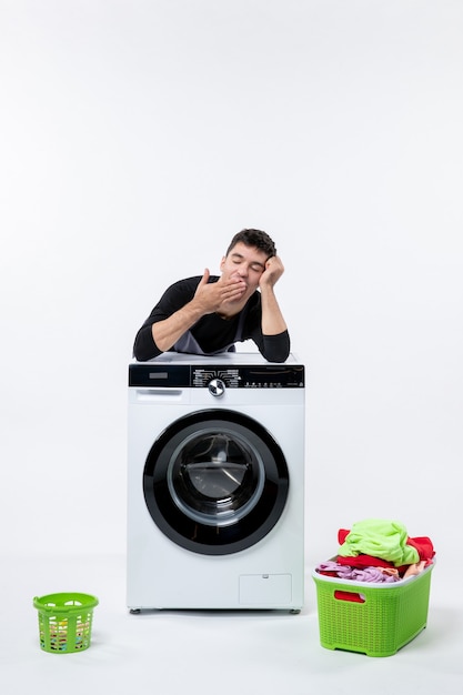 Vue de face du jeune homme avec lave-linge et vêtements sales sur mur blanc