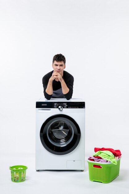 Vue de face du jeune homme avec lave-linge et vêtements sales sur mur blanc