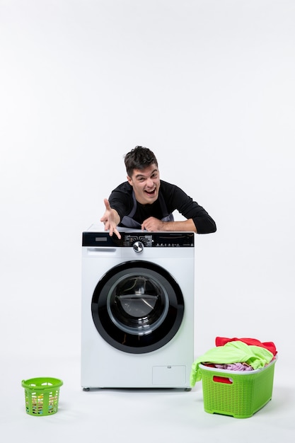 Vue de face du jeune homme avec lave-linge et vêtements sales sur mur blanc