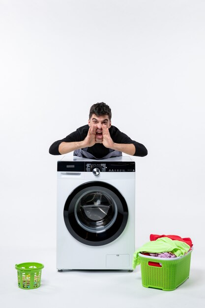 Vue de face du jeune homme avec lave-linge et vêtements sales sur mur blanc