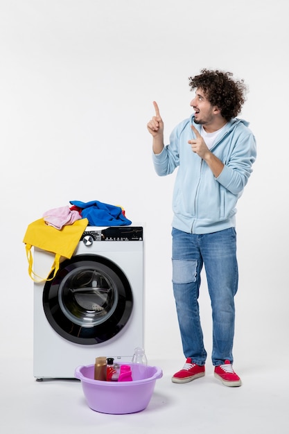 Vue de face du jeune homme avec lave-linge et vêtements sales sur mur blanc