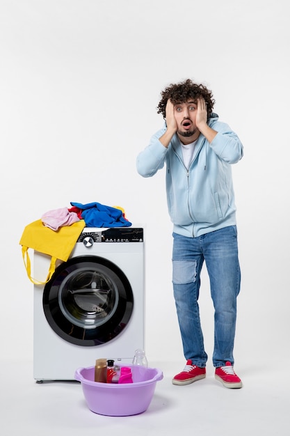 Vue de face du jeune homme avec lave-linge et vêtements sales sur mur blanc