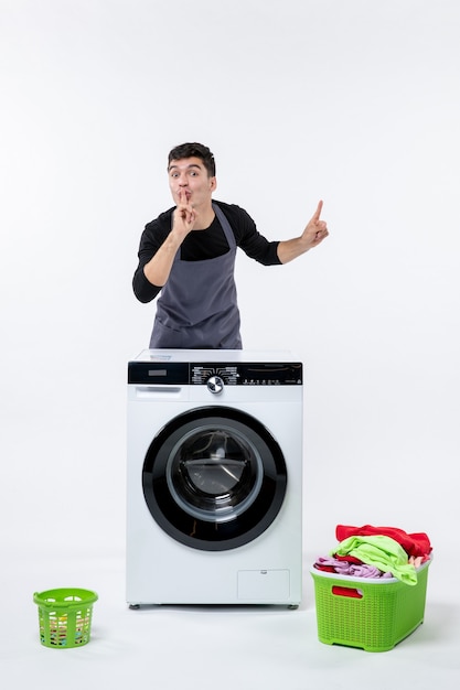 Vue de face du jeune homme avec lave-linge et vêtements sales sur mur blanc