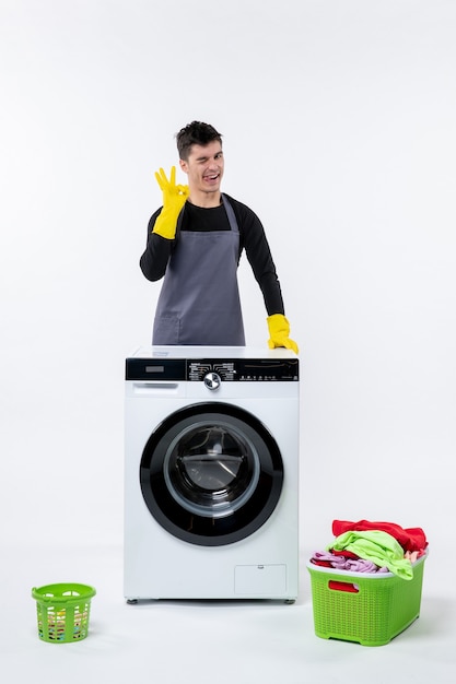 Vue de face du jeune homme avec machine à laver et vêtements sales sur mur blanc