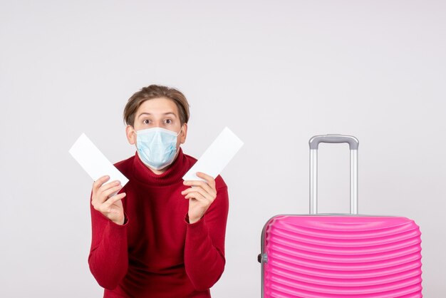 Vue de face du jeune homme en masque tenant des billets d'avion sur un mur blanc