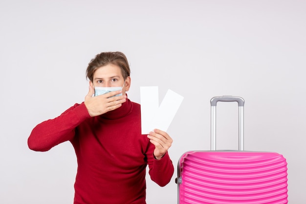 Vue de face du jeune homme en masque tenant des billets d'avion sur un mur blanc