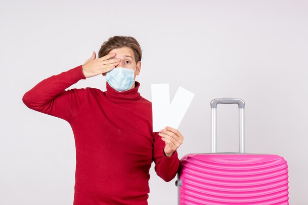 Vue de face du jeune homme en masque tenant des billets d'avion sur un mur blanc