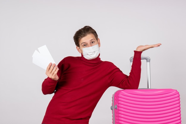 Vue de face du jeune homme en masque tenant des billets d'avion sur un mur blanc