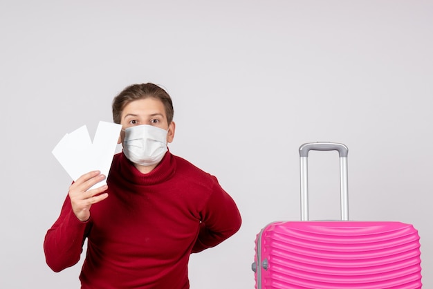 Photo gratuite vue de face du jeune homme en masque tenant des billets d'avion sur un mur blanc