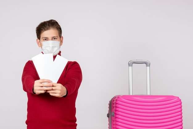 Vue de face du jeune homme en masque tenant des billets d'avion sur un mur blanc