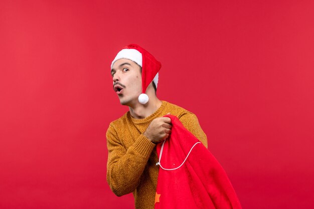 Vue de face du jeune homme ouvrant le sac présent sur le mur rouge