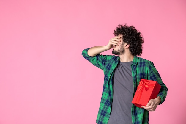 Vue de face du jeune homme avec paquet rouge sur mur rose clair