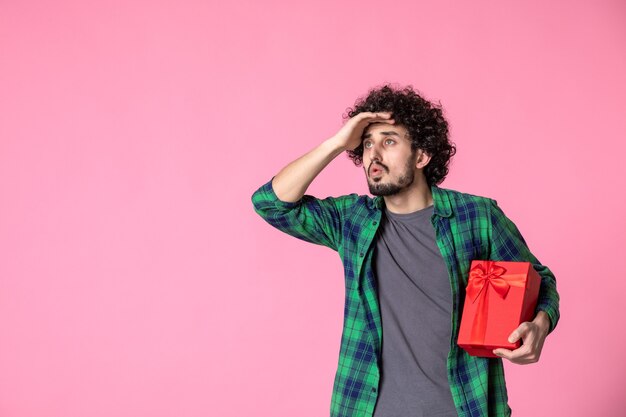 Vue de face du jeune homme avec paquet rouge sur mur rose clair