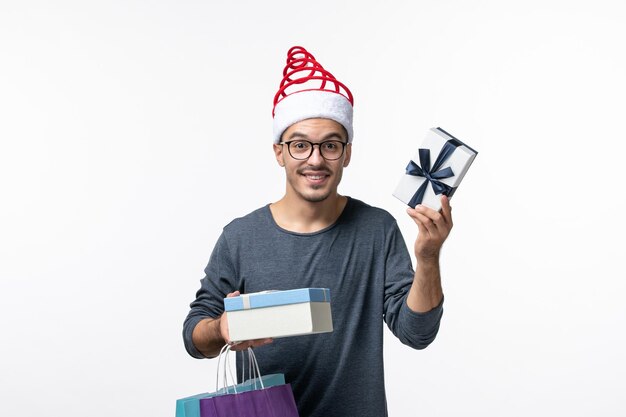 Vue de face du jeune homme avec des paquets et des cadeaux sur un mur blanc