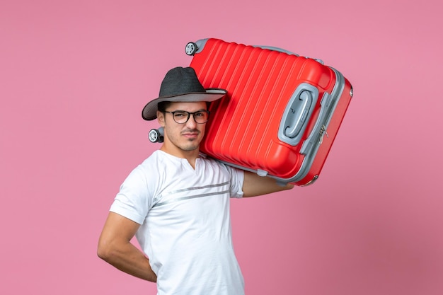 Vue de face du jeune homme partant en vacances et tenant un sac rouge sur le mur rose