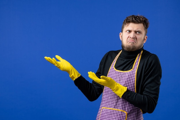 Vue de face du jeune homme perplexe debout sur le mur bleu