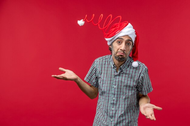 Vue de face du jeune homme portant une casquette de jouet drôle sur mur rouge