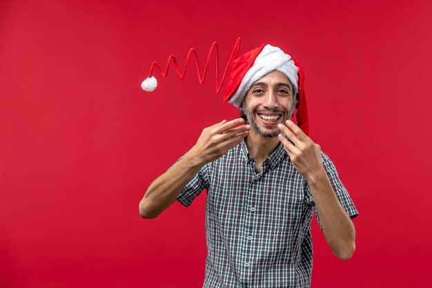 Vue de face du jeune homme portant un chapeau de jouet de Noël sur le mur rouge