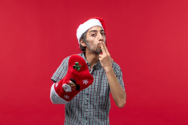 Vue de face du jeune homme portant des chaussettes de Noël sur le mur rouge