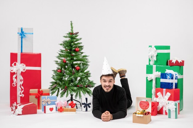 Vue de face du jeune homme portant joyeusement autour des cadeaux de vacances sur le mur blanc