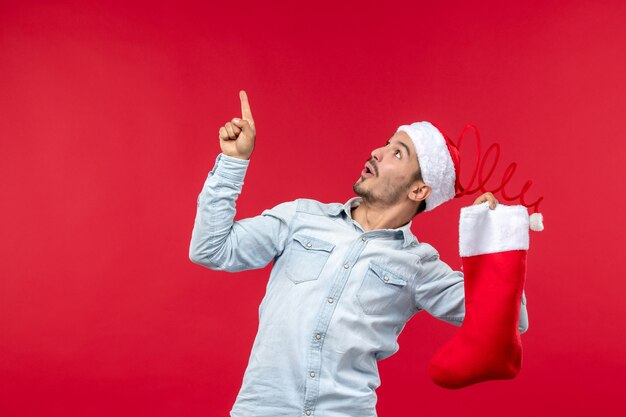 Vue de face du jeune homme posant avec chaussette de Noël sur mur rouge