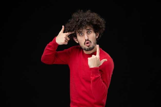 Vue de face du jeune homme en pull rouge sur le mur noir